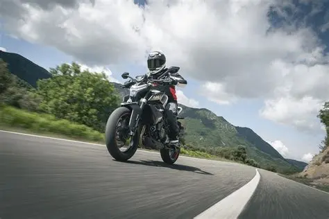 Piloto conduz CFMOTO 450NK preta em estrada sinuosa.