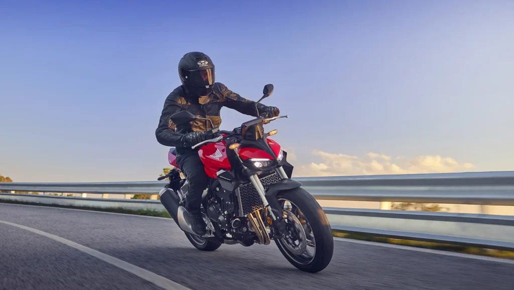 Piloto conduz Honda CB1000 Hornet Standard 2027 vermelha em estrada.