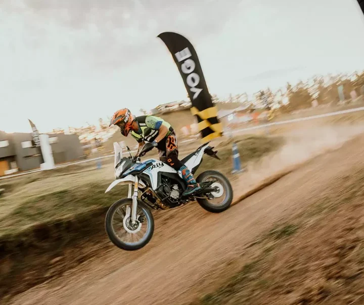 Piloto conduz VOGE 300 Rally branca e azul em trecho de terra.